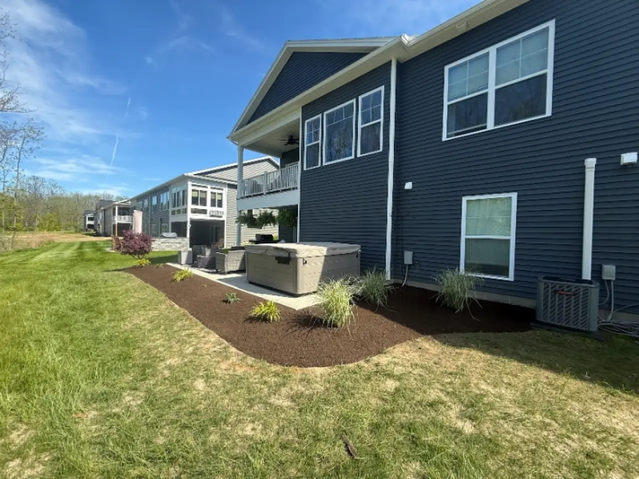 Dark blue house with fresh mulch, green grass, and a hot tub near the back patio.