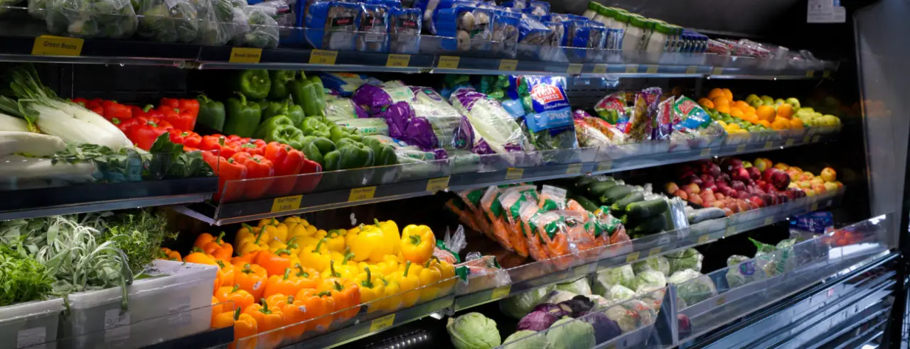 Colorful fresh vegetables, including peppers and lettuce, displayed on shelves in a grocery store.