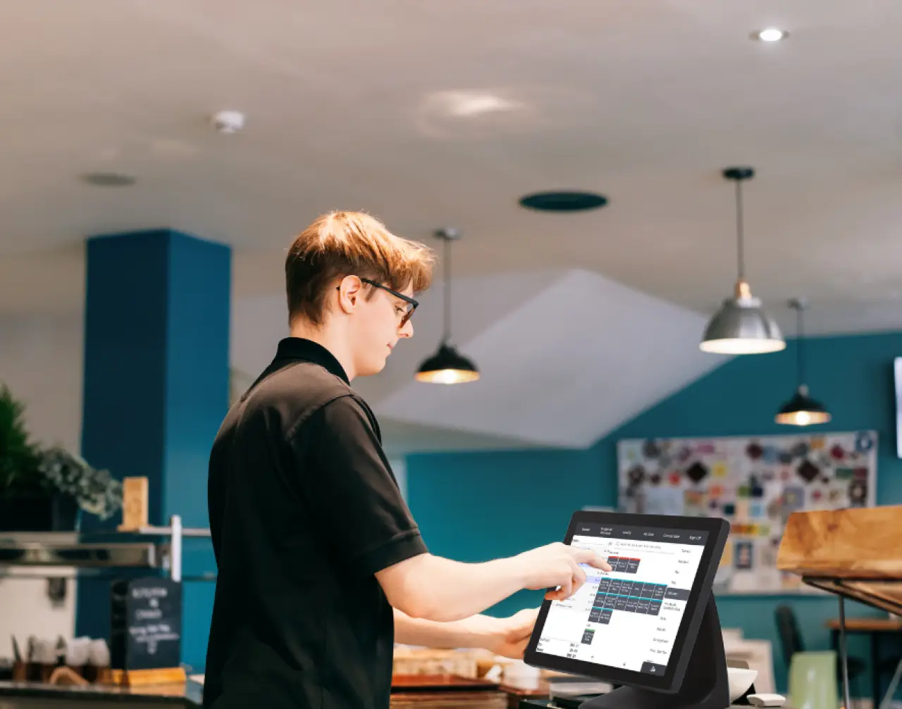 Person in black shirt using a touchscreen register at a modern café counter.