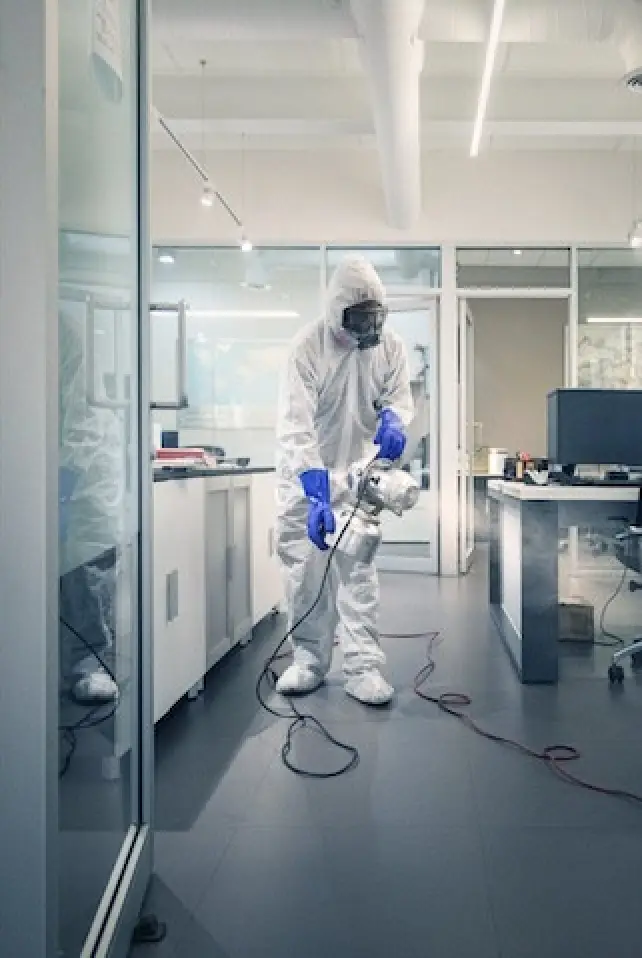 man in white PPE suit spraying cleaner