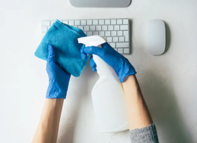 person wearing blue gloves spraying cleaner on cloth