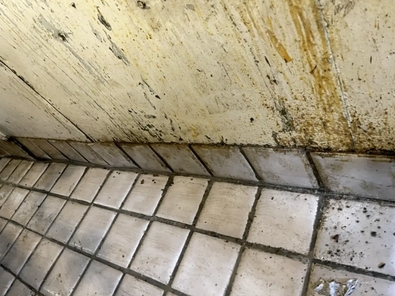 Dirty tiled floor and stained wall before cleaning.