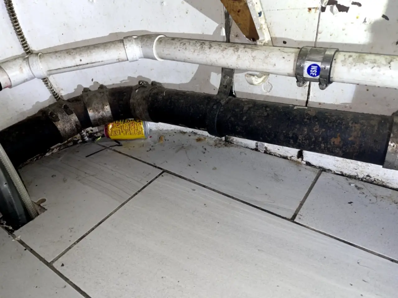 Soiled tiled utility area beneath exposed plumbing before cleaning.