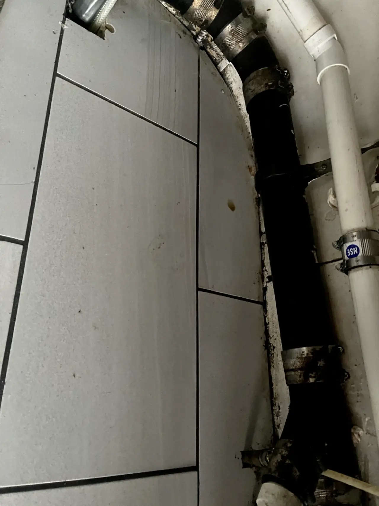 Grimy tiled surface surrounding exposed commercial plumbing.