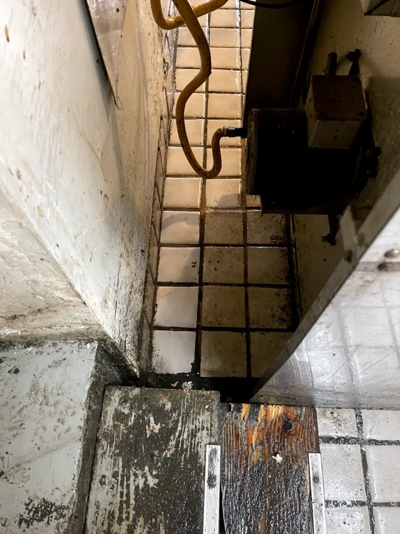 Stained tile floor and walls in a narrow utility area.