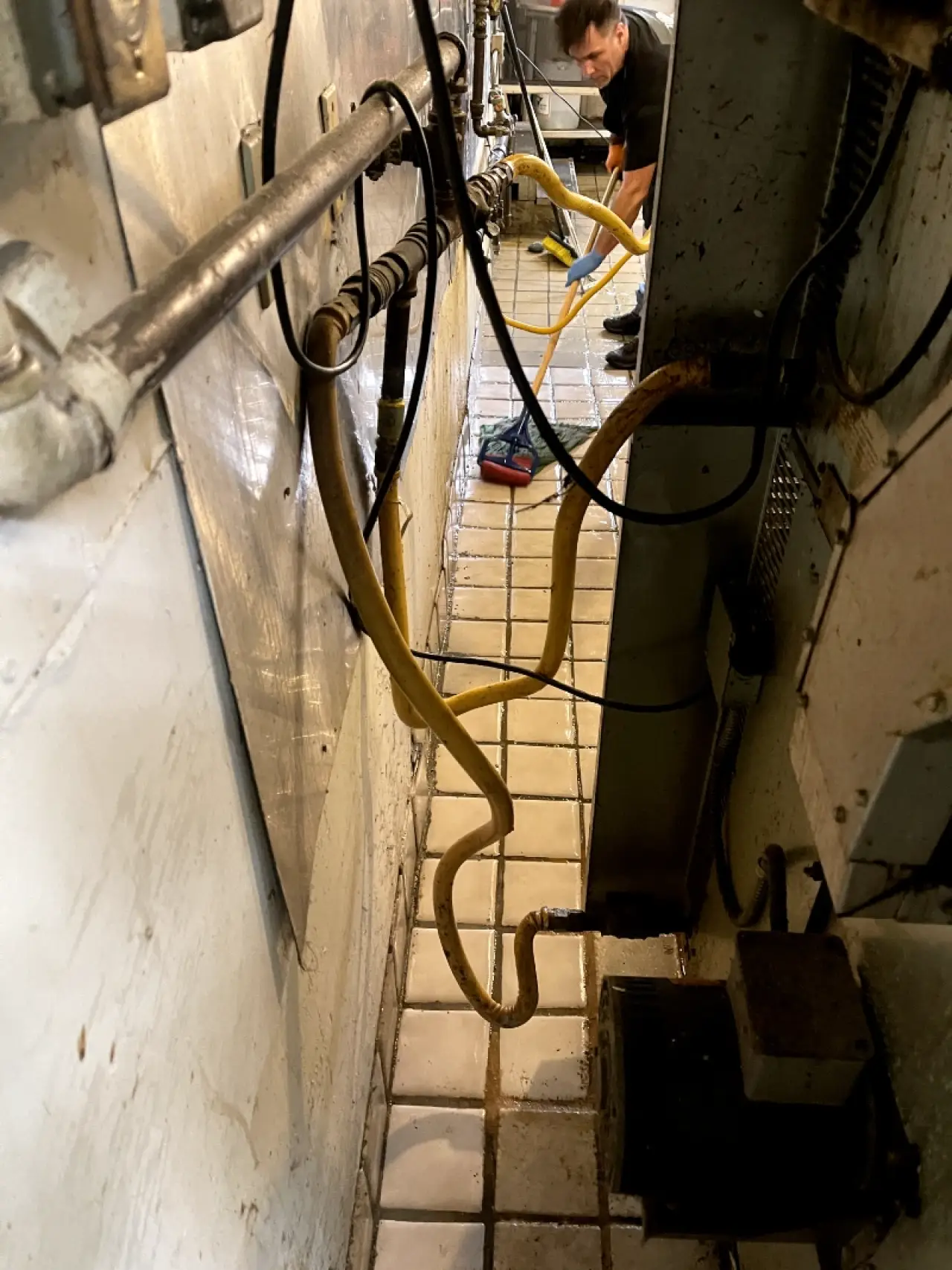Worker cleaning a tiled floor behind commercial kitchen equipment.