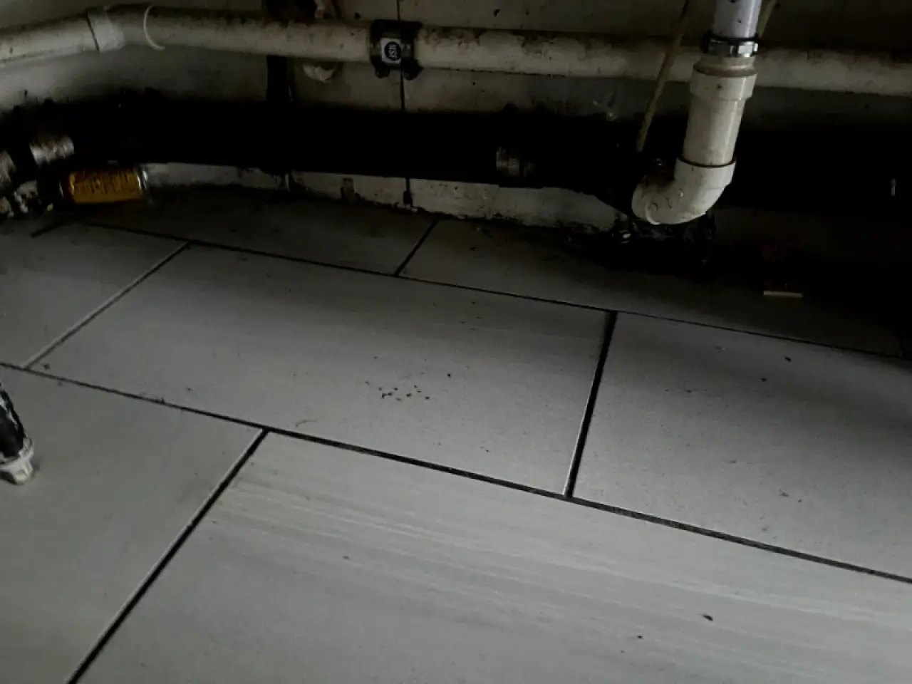 Tiled floor beneath exposed plumbing in a commercial facility.