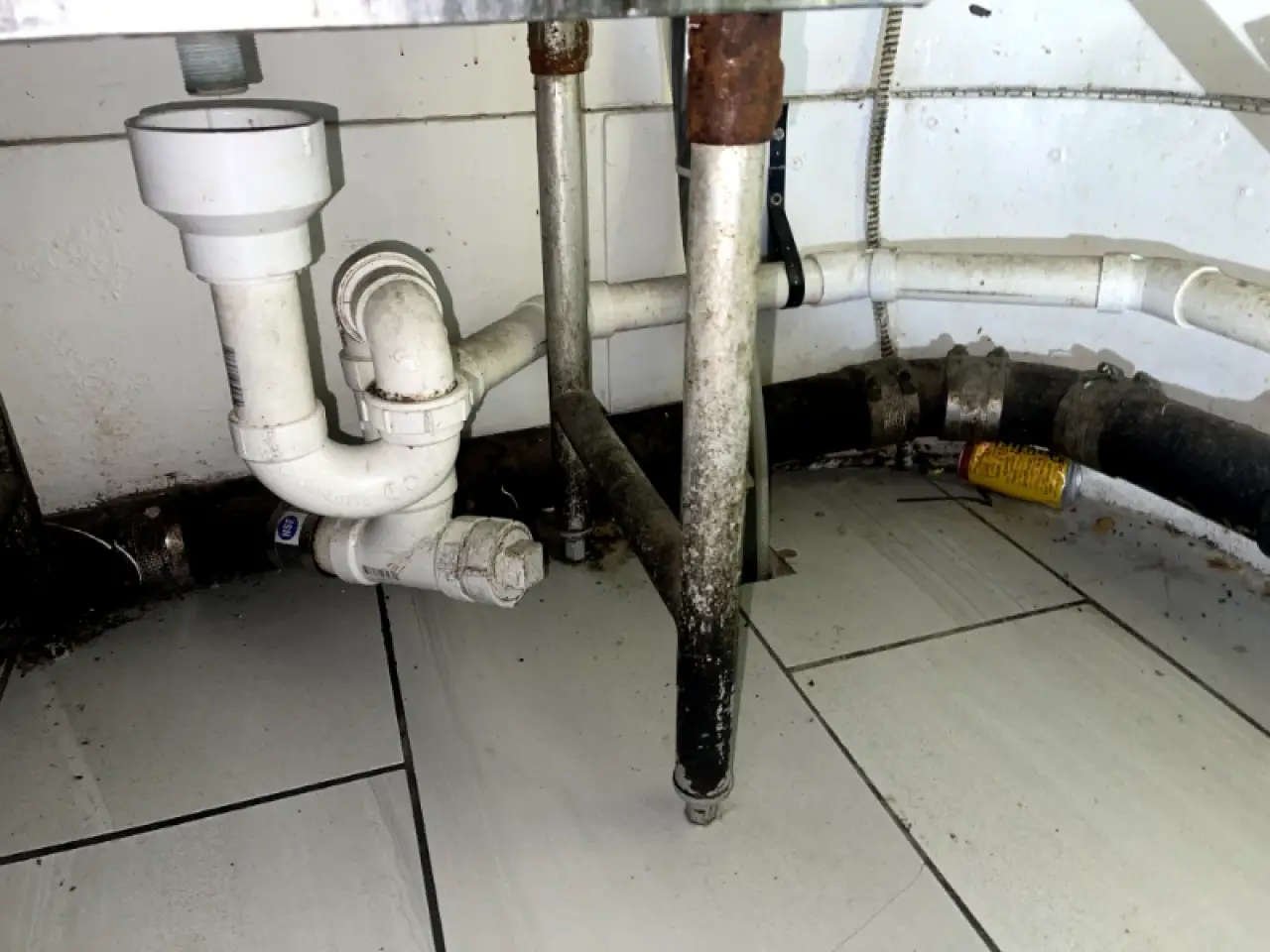 Stained plumbing and tiled floor beneath a commercial sink.