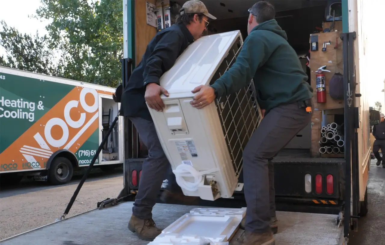 Two NOCO technicians unloading an air conditioning unit from a NOCO heating and cooling truck