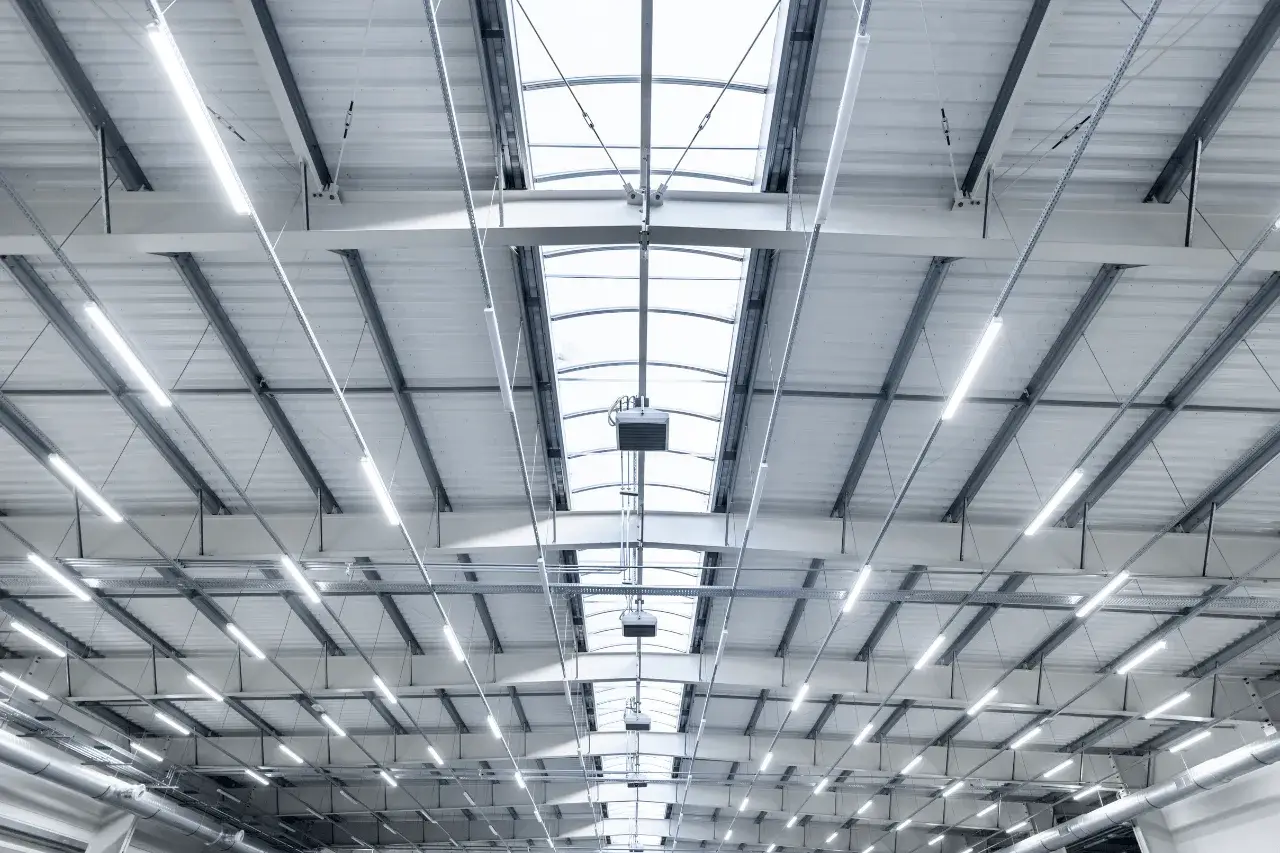 Modern industrial ceiling with metal beams, skylights, and bright overhead lighting.