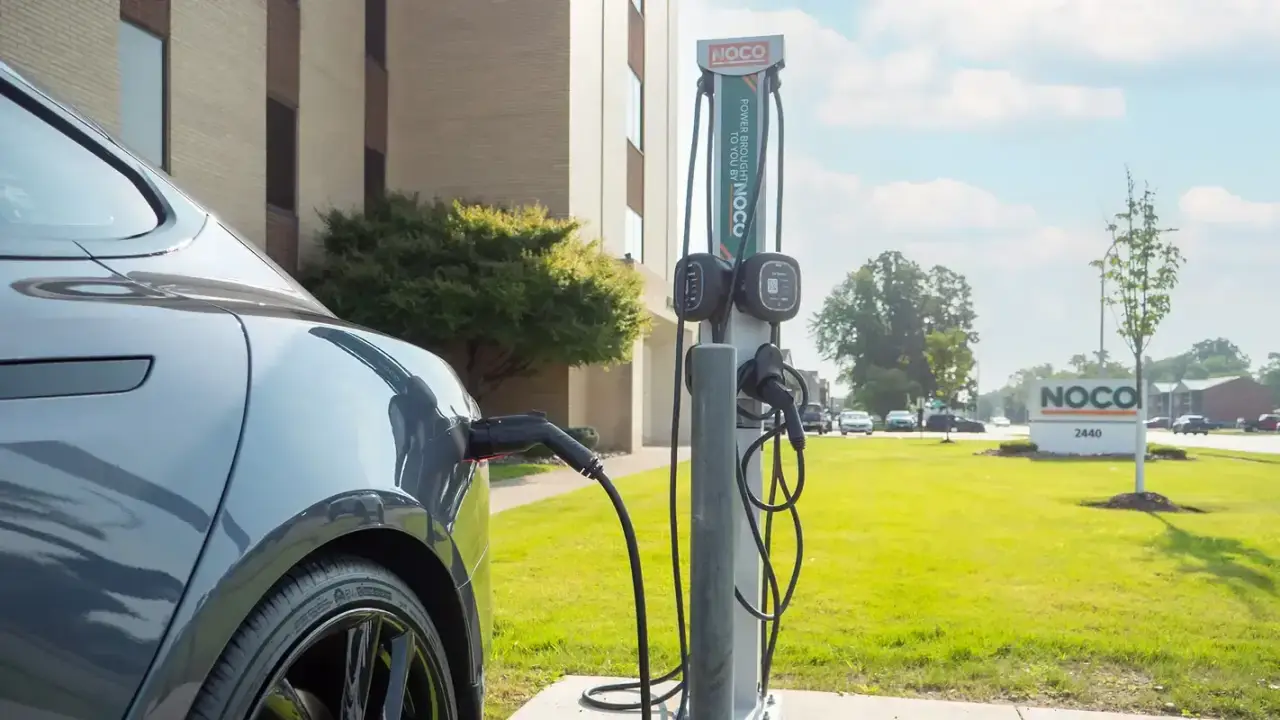 An electric car charging at a NOCO charging station outside a building on a sunny day.