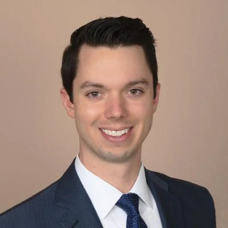 michael gerlach smiling man in a blue suit and tie against a plain beige background