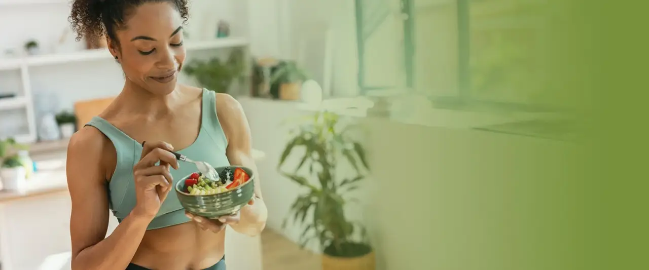 woman in workout attire eating a healthy salad in a bright, green-hued room