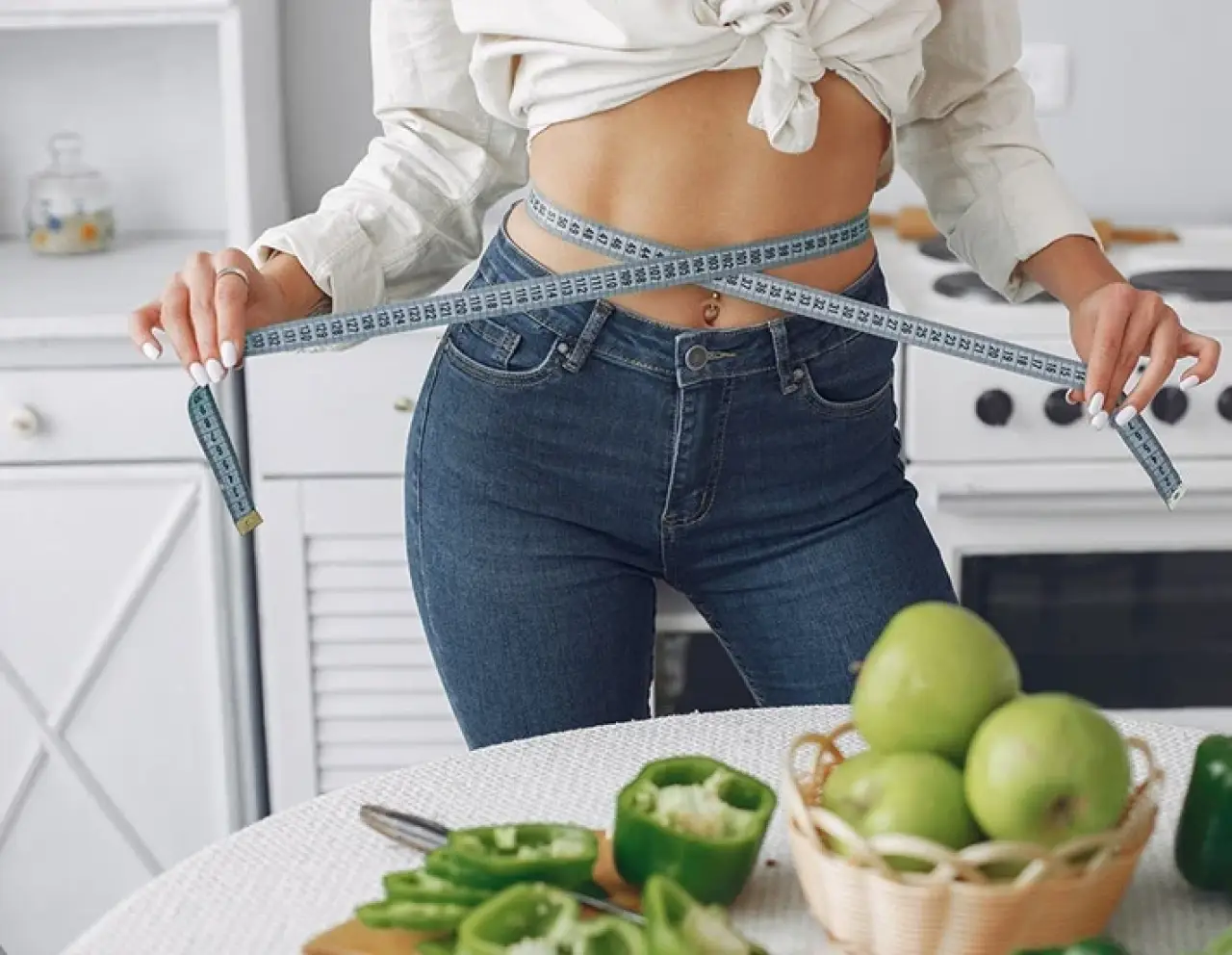 person measuring waist with tape in kitchen, healthy food on table