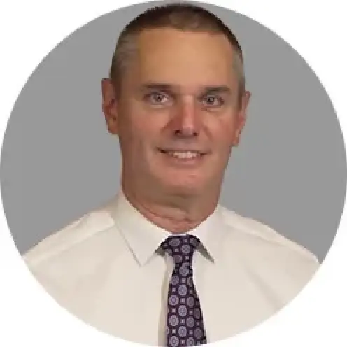 smiling man in a white shirt and patterned tie with a gray background