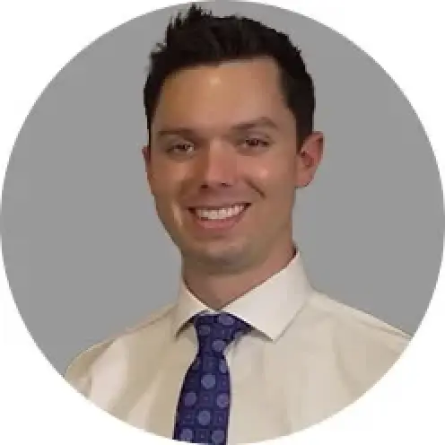 smiling man in a white shirt and blue patterned tie with a gray background