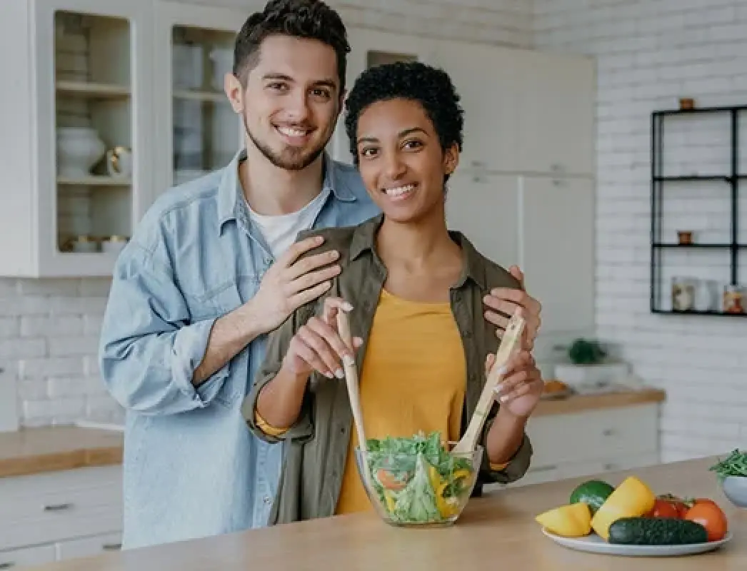 couple in kitchen making salad fresh vegetables on the counter beside them