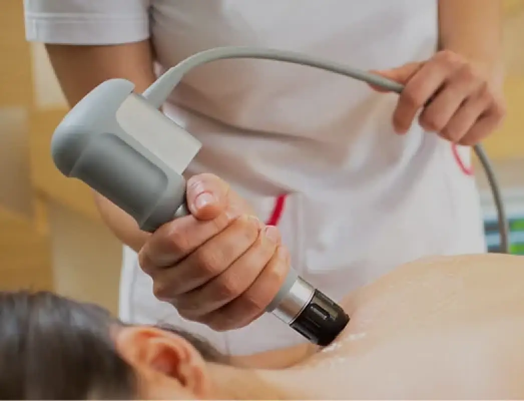 person using a handheld device for a treatment on a patients shoulder