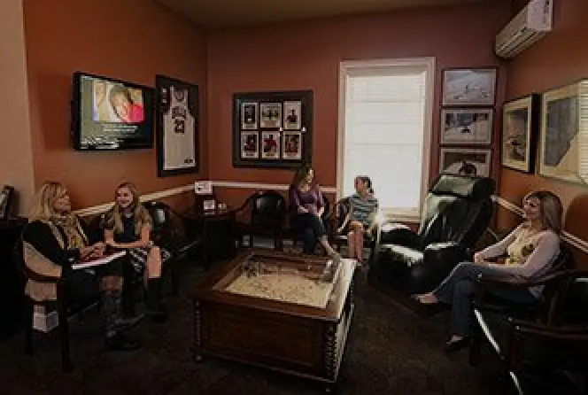 Five women sit and converse in a cozy, sports-themed waiting room with framed jerseys and photos.