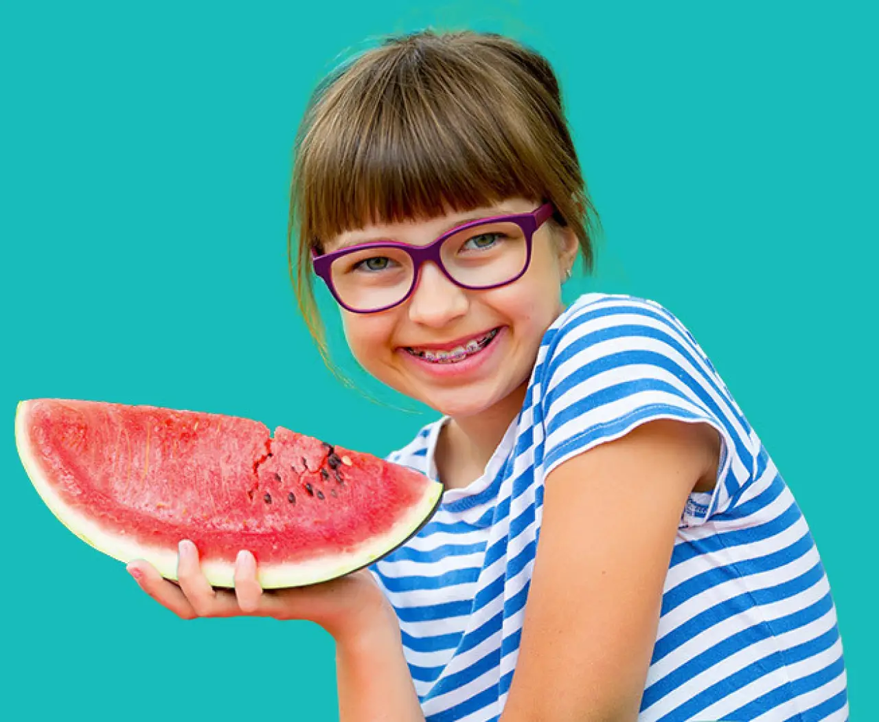 Smiling girl in glasses holds sliced watermelon against a solid teal background.