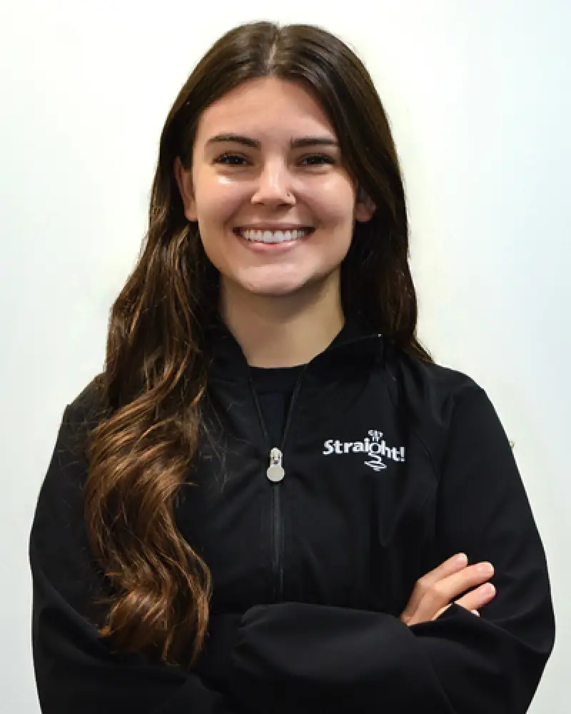 Smiling woman with long brown hair in a black Straight jacket, arms crossed.
