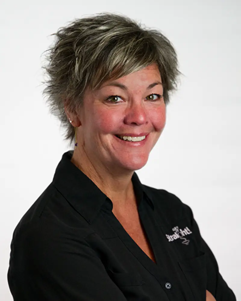 Smiling woman with short, light brown hair, wearing a black collared shirt on white background.