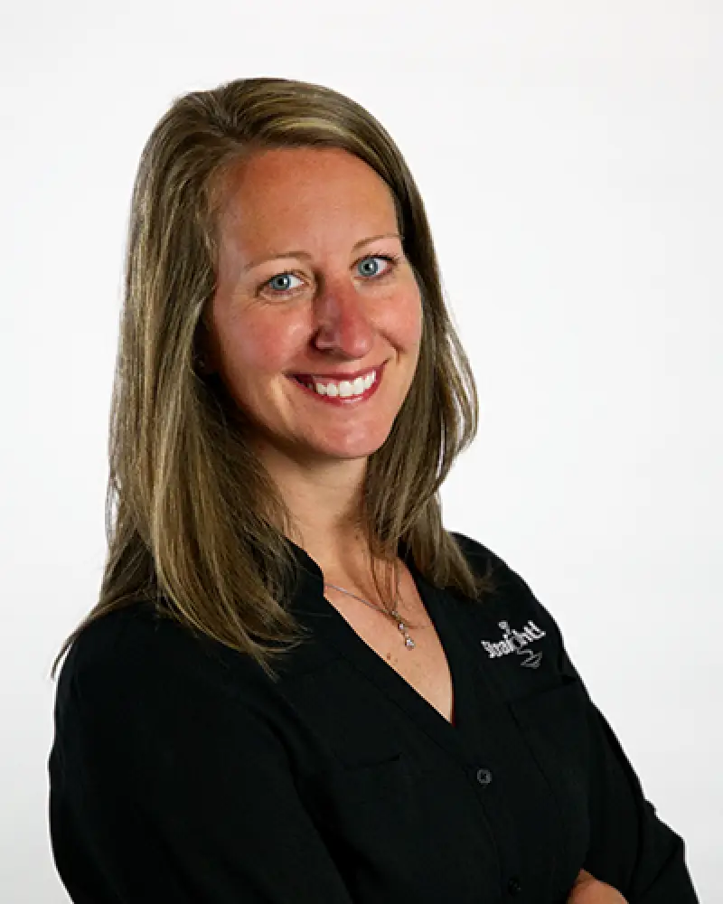 Smiling woman with long brown hair in a black shirt on a plain white background.