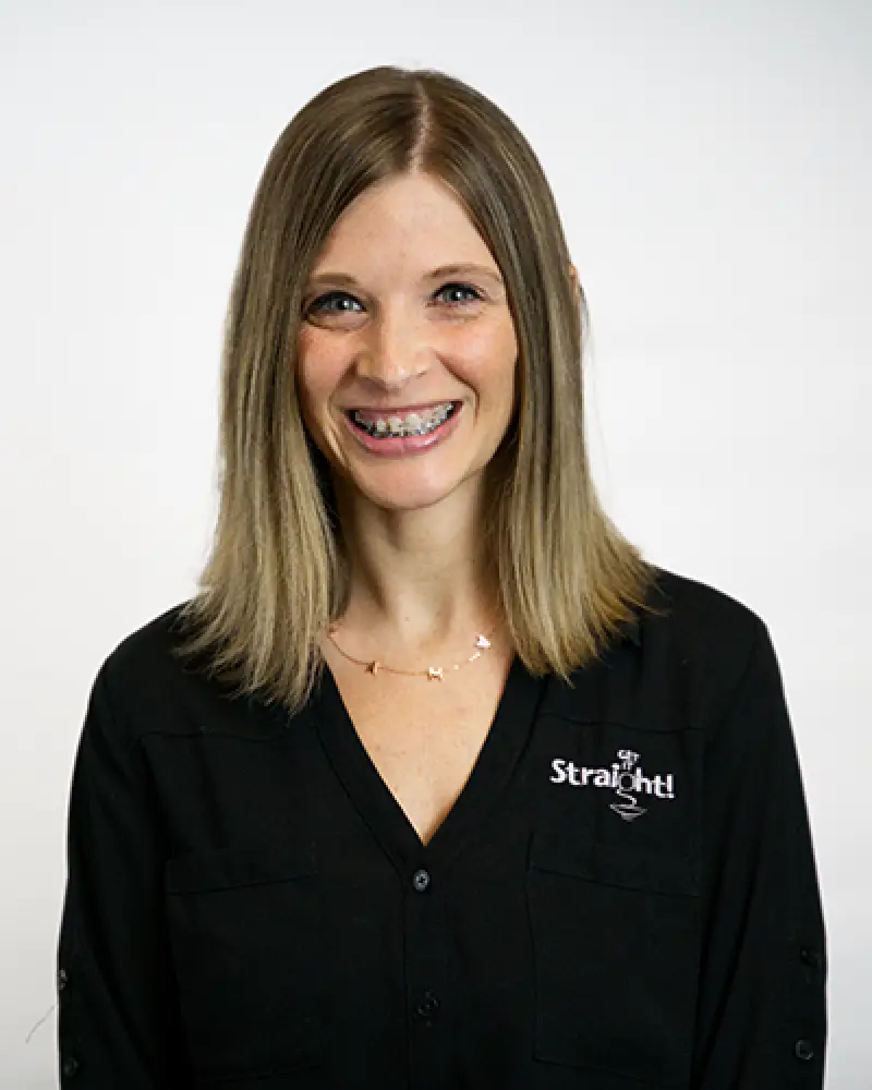 Smiling woman with braces, wearing a black shirt that says Straight on a plain background.