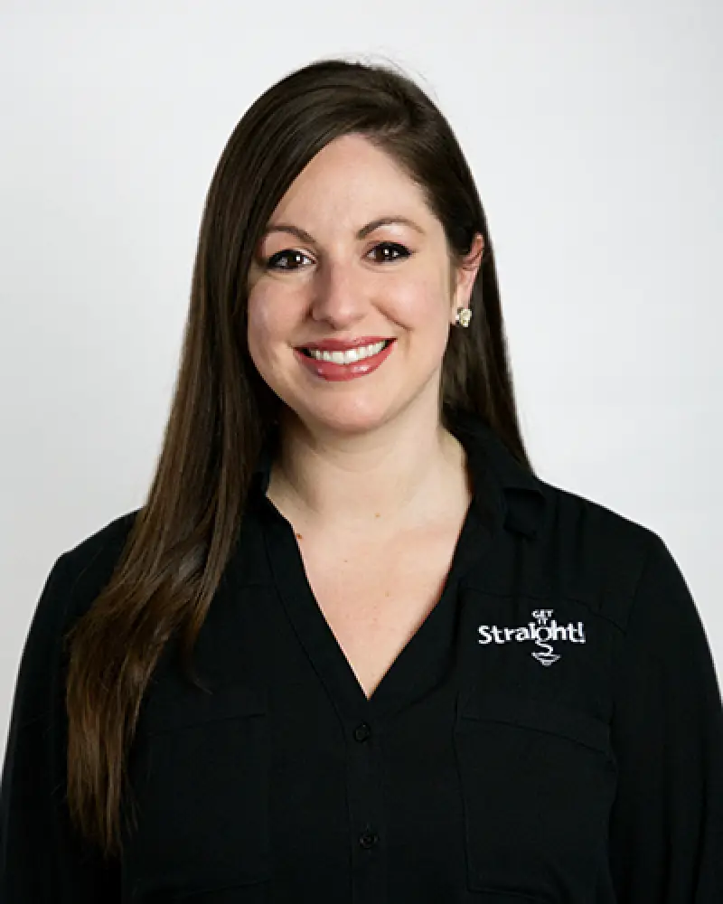 Woman with long brown hair, smiling, wearing a black Get Straight logo shirt, on white background.