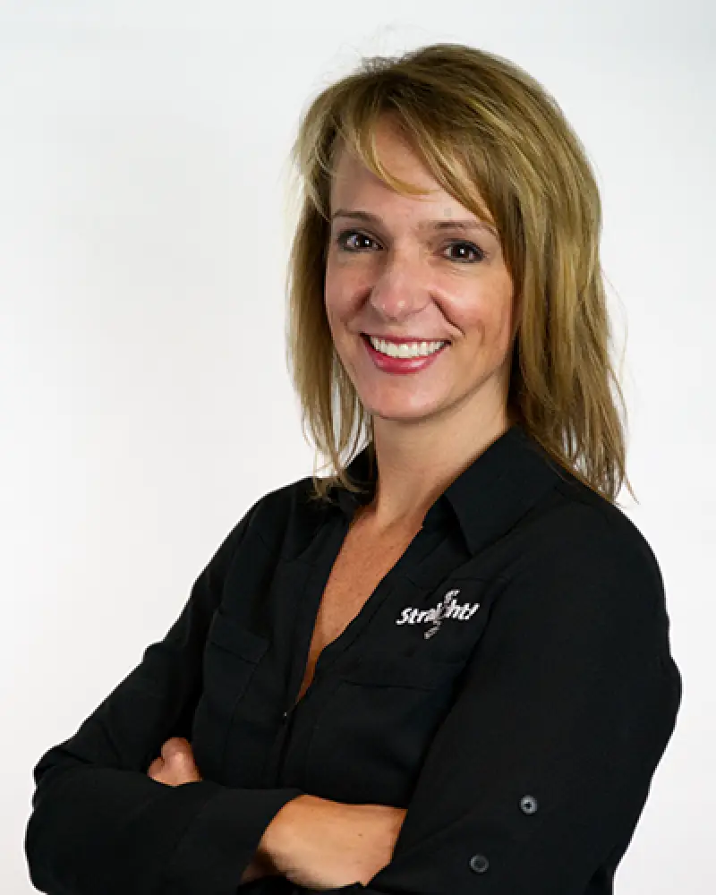Woman with blonde hair in a black shirt smiling with arms crossed against a white background.