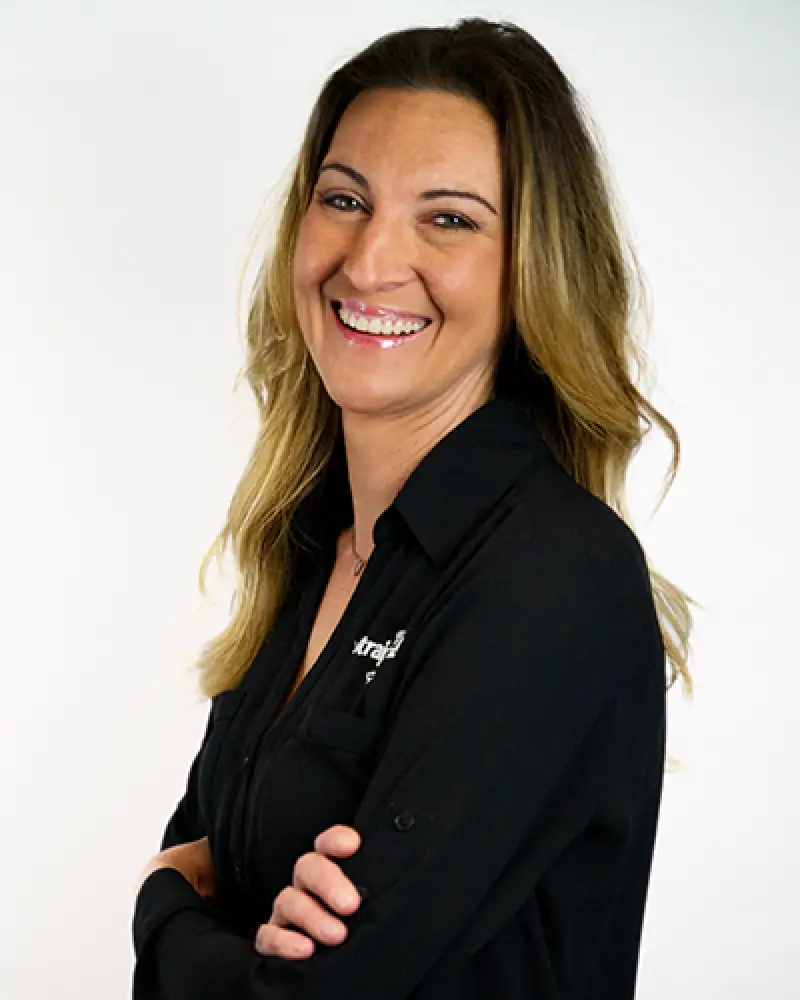 Woman with long brown hair smiling, wearing a black shirt, arms crossed, on a white background.