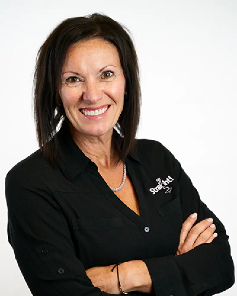 Woman with shoulder-length dark hair, smiling and standing with arms crossed in a black shirt.