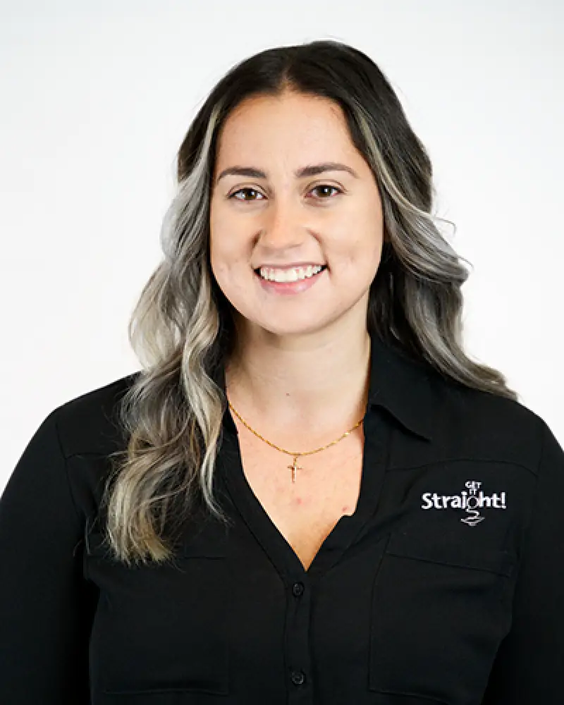 Woman with wavy hair smiling, wearing a black Get Straight shirt and gold necklace.