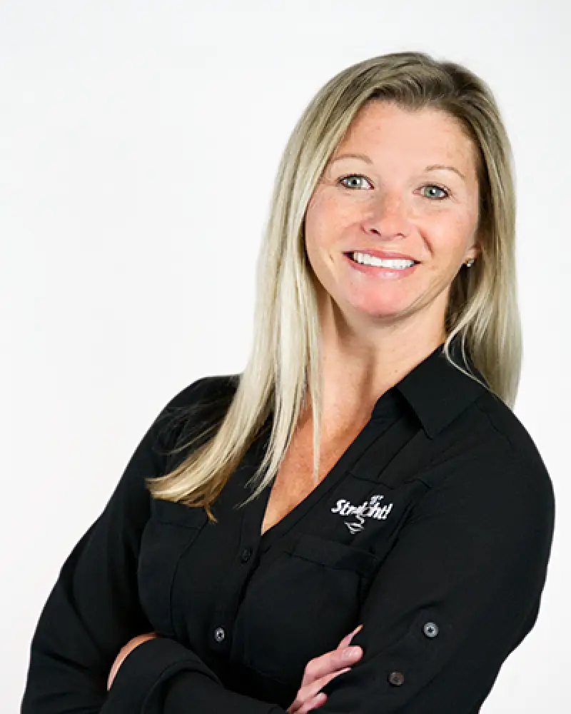 Smiling woman with long blonde hair in a black shirt, standing with arms crossed.