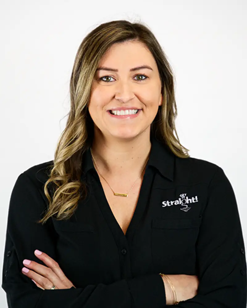 Woman with wavy hair in black shirt, smiling with arms crossed against a white background.