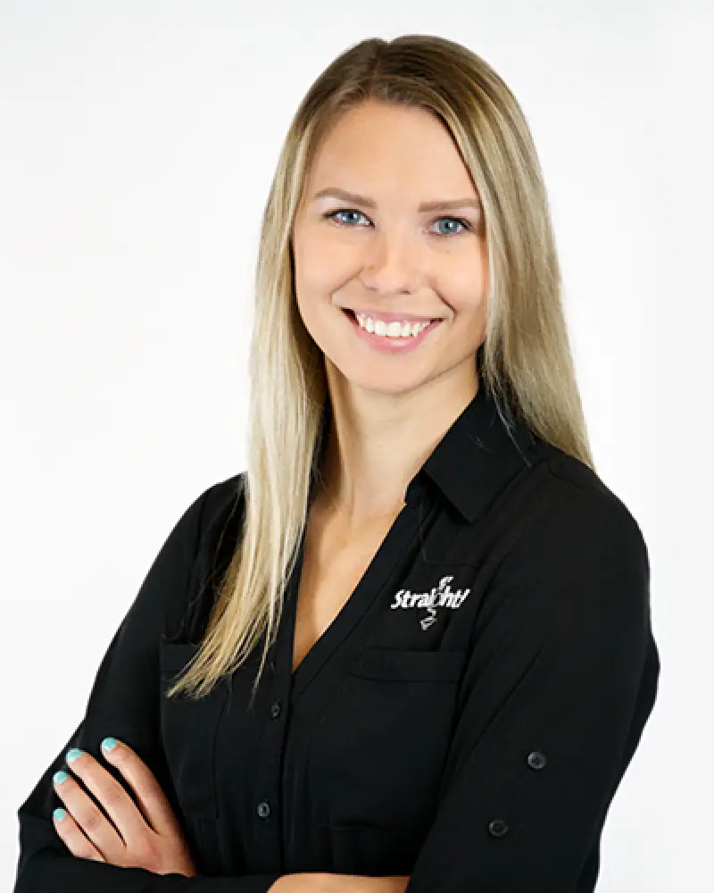 Woman with long blonde hair in a black shirt, arms crossed, smiling at the camera.