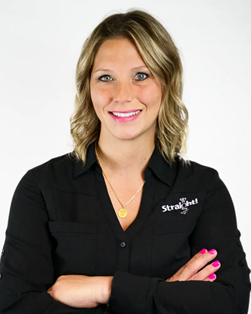 Woman with wavy blonde hair in a black shirt, smiling with arms crossed against white background.