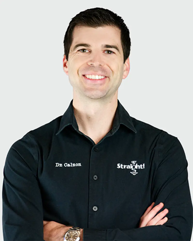 Smiling man in a black shirt with embroidered text, arms crossed, on a light background.