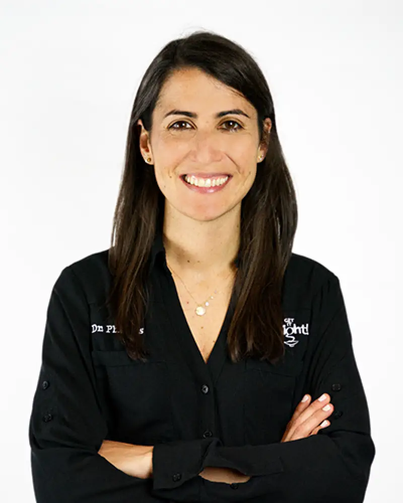 Woman with long dark hair smiling, arms crossed, wearing a black shirt on a white background.