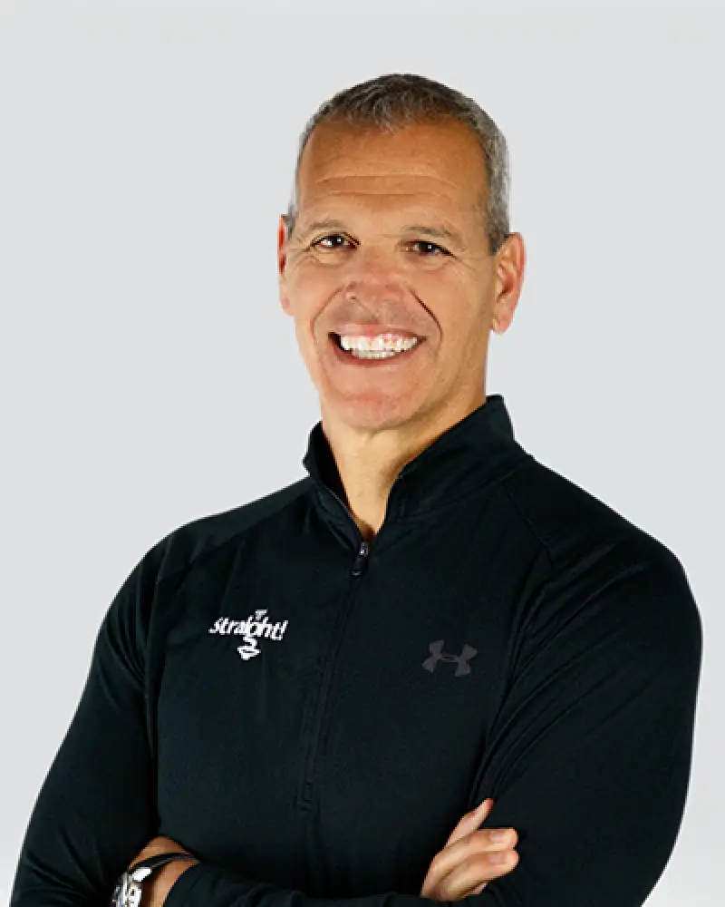 Smiling man in a black zip-up Under Armour top standing with arms crossed against a light background.