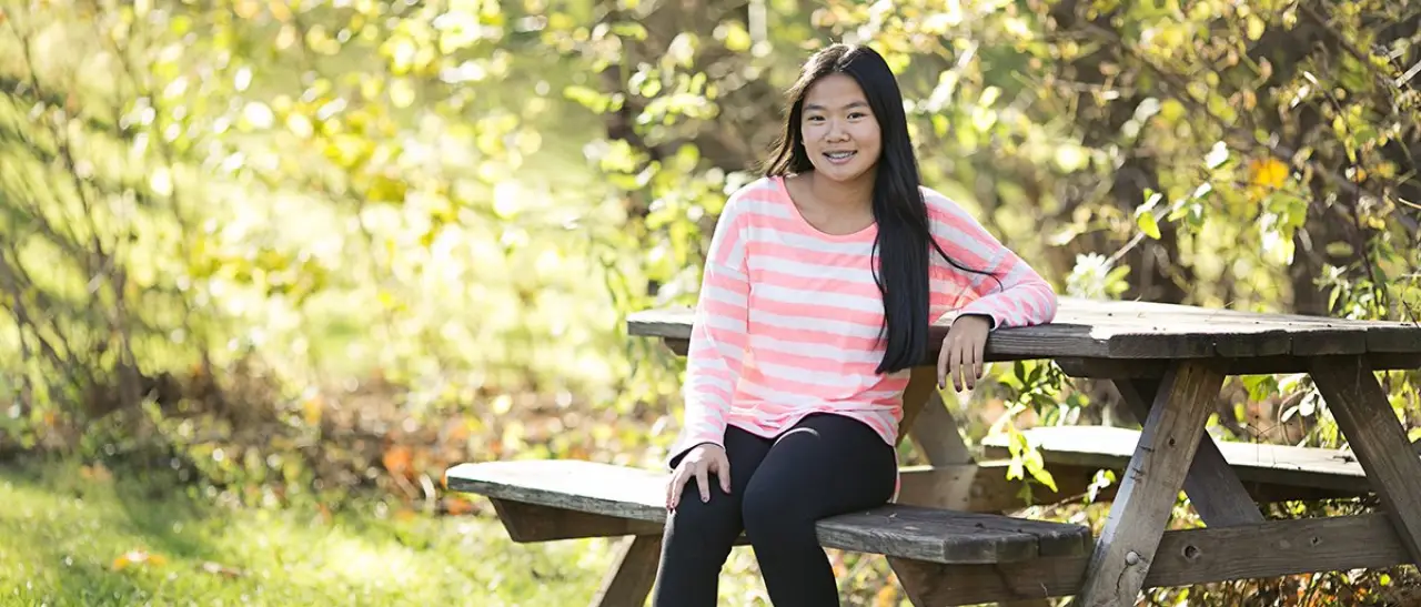 Girl in a pink striped shirt with braces smiling and sitting on a bench