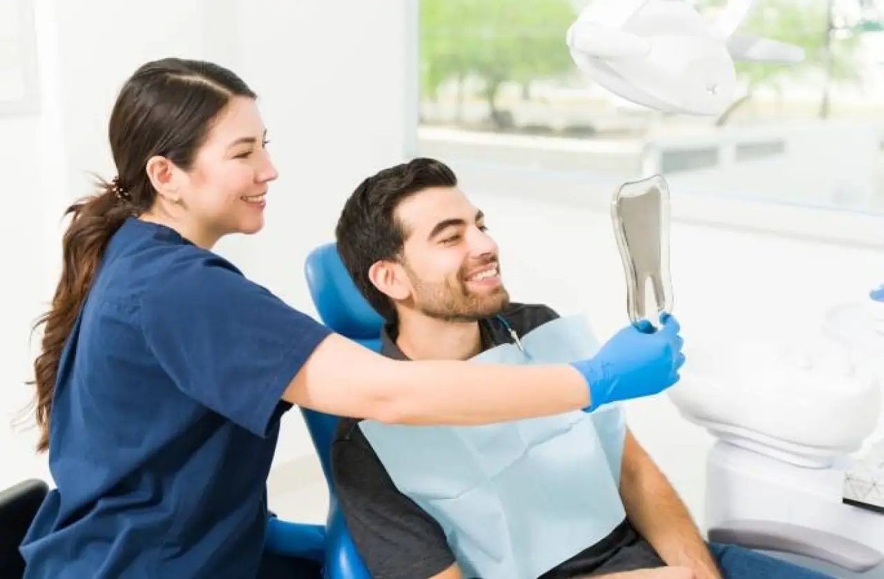 A dentist shows a smiling patient his reflection in a handheld mirror at the clinic.