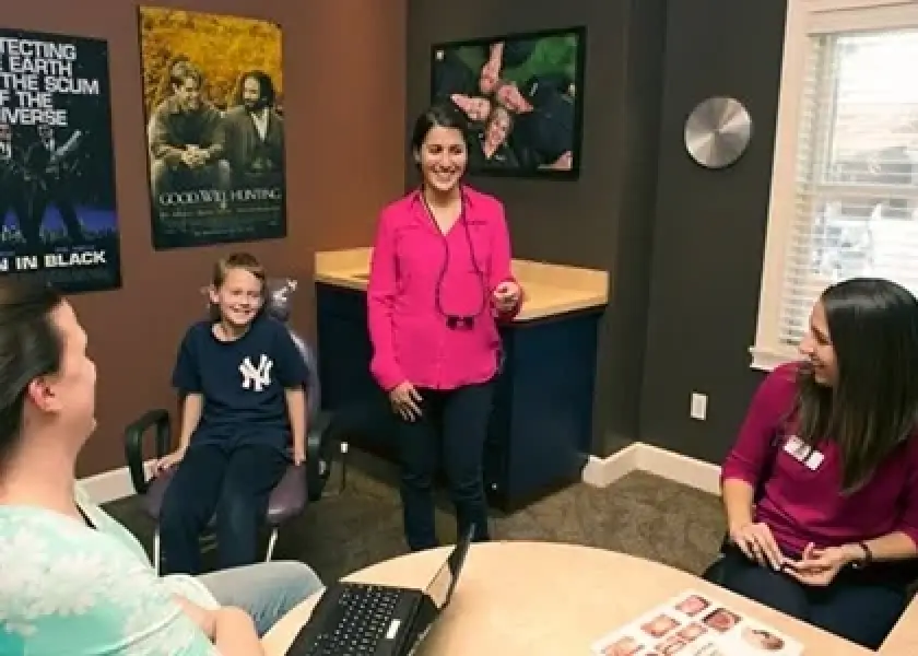 A dentist and three patients smile and talk together in a dental office with movie posters.
