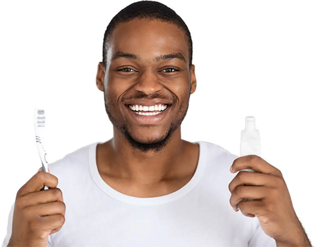 Smiling man in white shirt holding a toothbrush in one hand and toothpaste in the other.