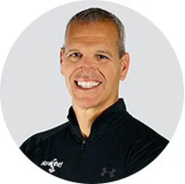 Smiling man with short gray hair in a black zip-up jacket against a light gray background.