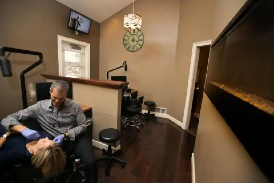 A dentist examines a patient in a modern, warmly lit dental office with brown walls.