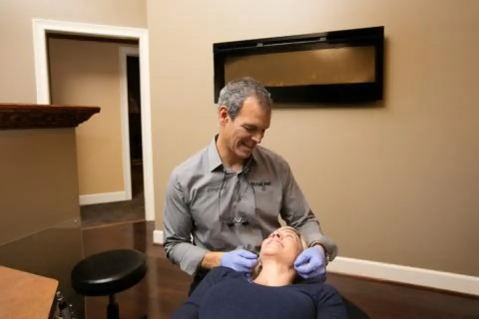 A dentist wearing gloves examines a smiling patient in a warmly lit dental office.