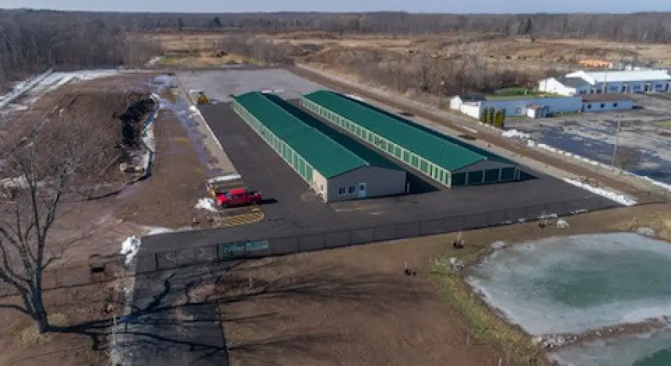 Aerial view of a storage facility with green roofs, a red truck, and surrounding empty lots.