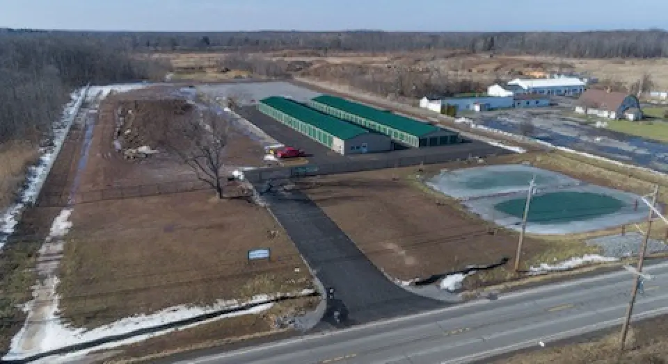 Aerial view of a storage facility with green doors, near a main road and open fields.