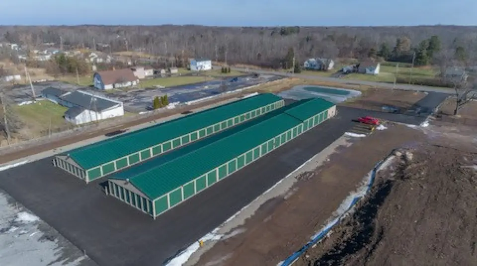 Aerial view of green-roofed storage units on a paved lot, surrounded by trees and houses.
